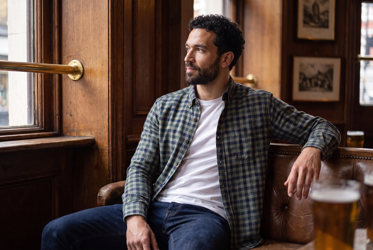 Man in a green and navy brushed cotton check shirt over a white tee in a London pub
